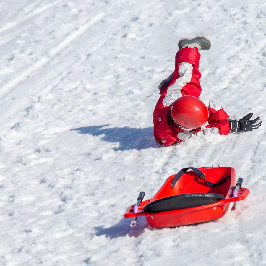 child lying on snow after sled accident